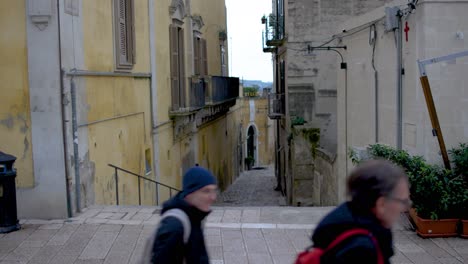 Alley-in-Matera,-Italy-with-people-walking-by-in-an-establishing-video-shot