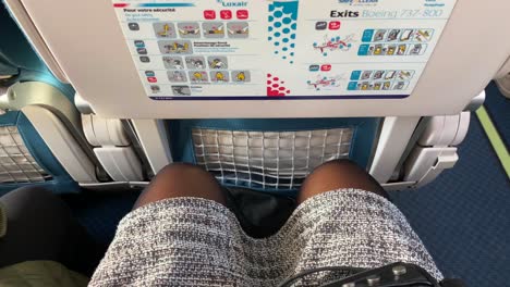 Traveling-in-tight-airplane-seat-with-very-little-legroom-in-Luxair-airlines,-female-legs-and-knees-squeezed-tight-on-a-Boeing-aircraft,-uncomfortable-seat,-4K-shot