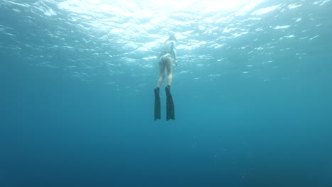 Female-freediver-fins-up-to-surface-of-clear-blue-ocean,-cinematic-slow-motion