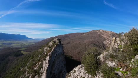 FPV-drone-aerial-image-taken-from-the-top-of-a-towering-stone-mountain,-a-calming-natural-image-with-shades-of-green,-grey,-and-blue-sky