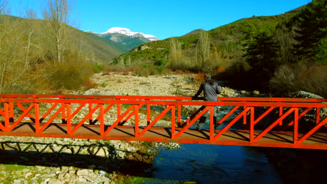 Aerial-view-of-a-man-standing-in-a-mountain-red-bridge-contemplating-the-landscape-of-the-Spanish-Pyrenees