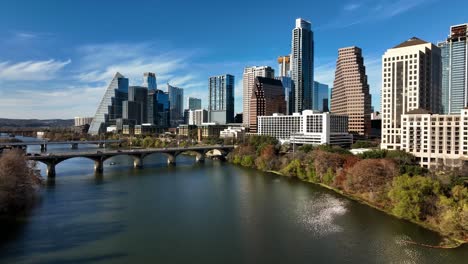 Aerial-view-low-over-the-river,-towards-high-rise,-sunny,-fall-day-in-Austin,-USA