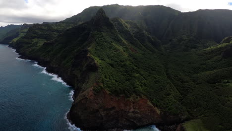 Vista-Aérea-De-La-Costa-Azul-Y-Las-Olas-Rompiendo-A-Lo-Largo-De-Las-Colinas-Ondulantes-En-Kauai-Hawaii