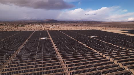 Aerial-Drone-Footage-of-Solar-Panel-Field-in-Joshua-Tree-National-Park-on-a-Sunny-Day-with-rainbow-in-the-background,-horizontal-pan-moving-backwards