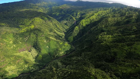 Aerial-View-of-Rolling-Hills-and-Green-Landscape-with-Waterfall-in-Distance-in-Kauai-Hawaii