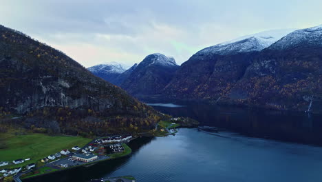 Aerial-flyover-Fjord-with-small-village-on-shore-and-snowy-mountain-peaks-in-background