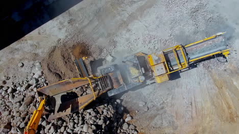 Excavator-loading-large-rocks-into-a-stone-crusher-to-make-gravel---spinning-aerial-view
