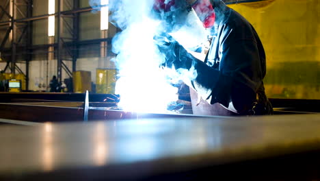 Man-wearing-protective-helmet-and-gloves-welding-in-big-workshop