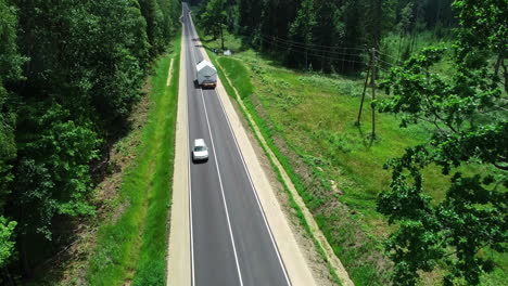 Aerial-tracking-shot-of-truck-transporting-prefabricated-house-on-road-between-forest-trees-during-summer