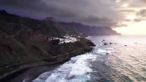 Aerial-view-of-car-drive-near-village-on-volcanic-green-coast-at-sunset,-Tenerife