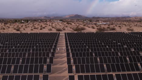 Aerial-Drone-Footage-of-Solar-Panel-Field-in-Joshua-Tree-National-Park-on-a-Sunny-Day-with-rainbow-in-the-background,-fast-horizontal-pan-zoom