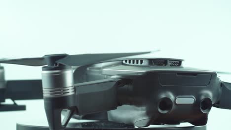 Nahaufnahme-Einer-Drohne-Mit-Kameraobjektiv-Und-Propellern,-Silbergraue-Farbe,-Auf-Einem-Rotierenden-360-Ständer,-Zeitlupe,-Studiobeleuchtung,-4k-Video