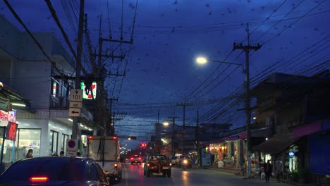 Vista-De-La-Calle-De-Tailandia-Paisaje-Urbano-Mientras-Los-Pájaros-Pululan-Y-Se-Posan-En-Las-Líneas-Eléctricas-Por-La-Noche