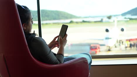 Mujer-Esperando-El-Avión-De-Salida-Volar-En-El-Aeropuerto-Sosteniendo-El-Teléfono-Mientras-Está-Sentado
