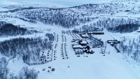 Iconic-hotel-building-in-winter-mountain-landscape-with-many-dog-homes-nearby,-aerial-view