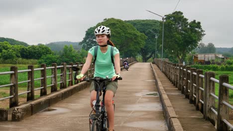 Asian-adult-woman-riding-and-pedaling-bike-towards-camera-on-bridge-in-Thailand
