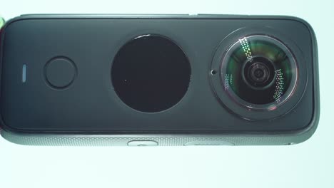 Eine-Vertikale-Nahaufnahme-Einer-360-Grad-Kamera-Mit-Doppelobjektiv,-Zwei-Objektivabdeckungen,-Glänzende-Studiobeleuchtung,-Runder-Bildschirm,-Funktionstaste,-Auf-Einem-Drehbaren-Ständer,-Zeitlupe,-4k-Video