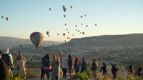 Tourists-in-Cappadocia,-Turkey-Watching-Hot-Air-Balloons-Flying-Above-Landscape