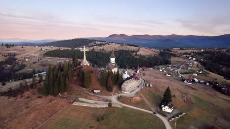 Aerial-view-of-a-church-on-top-of-a-hill-in-alpine-landscape-at-sunset