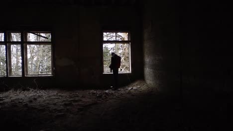 Silhouette-of-a-man-inside-of-an-abandoned-hospital-looking-out-of-the-window