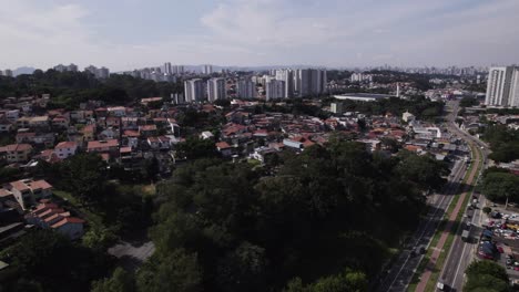 Die-Drohne-Bewegt-Sich-Nach-Oben-Und-Vorne-Und-Enthüllt-Die-Skylane-Von-São-Paulo-City-Im-Hintergrund-Und-Eine-Belebte-Straße-Rechts
