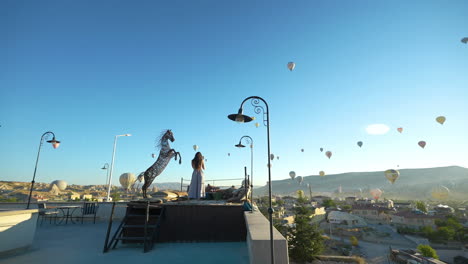 Frau-Auf-Der-Terrasse-Mit-Blick-Auf-Die-Landschaft-Von-Kappadokien-Und-Heißluftballons,-Türkei