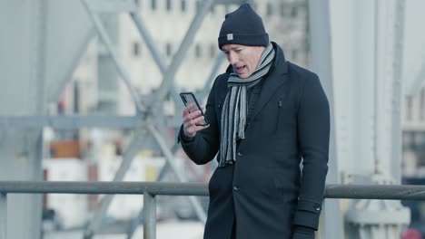 Man-facetiming-outside-in-the-cold-city-wearing-his-winter-clothes-in-the-soft-daylight