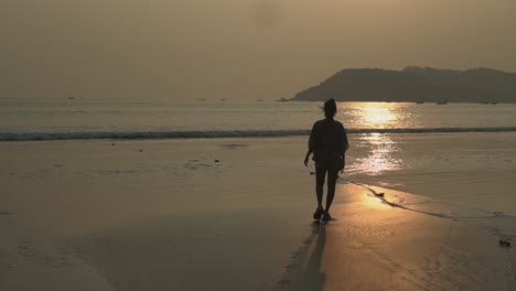 Landschaftsansicht-Einer-Jungen-Frau,-Die-Bei-Sonnenuntergang-An-Einem-Sandstrand-In-Richtung-Meer-Geht