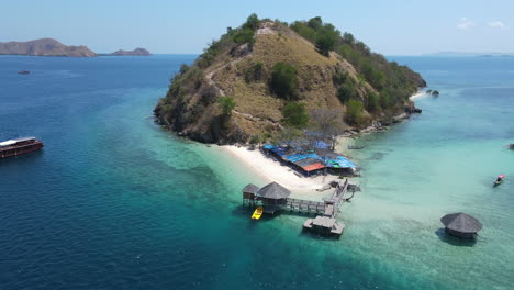 Islas-De-Komodo,-Indonesia,-Vista-Aérea-Del-Muelle-De-Madera,-Playa-De-Arena-Blanca-Y-Turista,-Revelando-Disparos-De-Drones