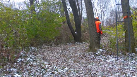 Hunter-dressed-in-orange-and-camouflage-walking-along-a-game-trail-in-early-inter-in-American-Midwest