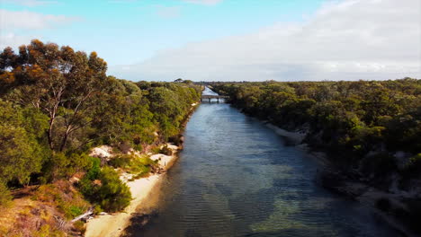 Vista-De-Drones-Río-Cristalino-Que-Fluye-A-Través-De-Un-Pequeño-Valle-Boscoso-Con-Un-Puente-En-Un-Día-Parcialmente-Nublado