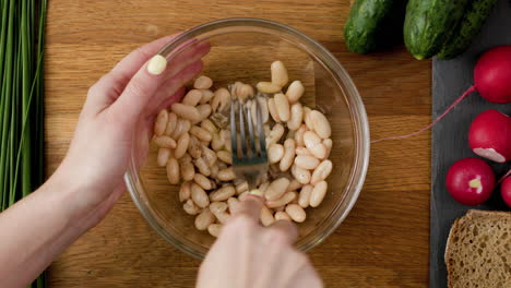 Mashing-white-beans-with-a-fork-to-prepare-vegan-sandwich-spread-with-rye-bread,-seasoned-with-salt,-pepper-and-olive-oil