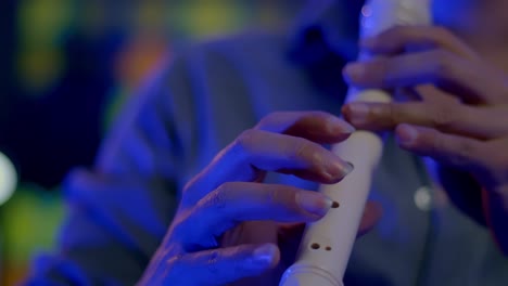 Slow-Motion-Shot-Of-Musician-Playing-Recorder,-Blurry-Colorful-Lights-In-Background