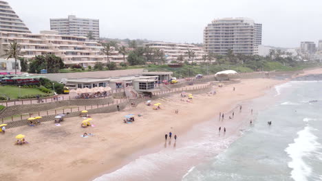 Aerial-drone-shot-along-Umhlanga-main-beach-with-people-sitting-under-umbrellas