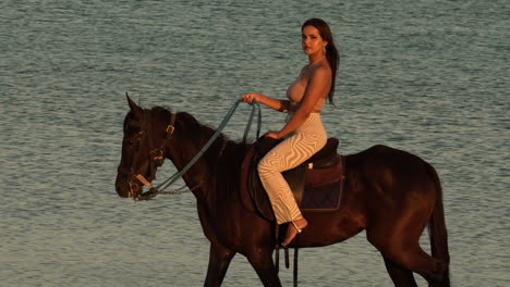 Schöne-Elegante-Junge-Frau,-Die-Auf-Einem-Schwarzen-Pferd-Reitet,-Mit-Dem-Meer-Im-Hintergrund