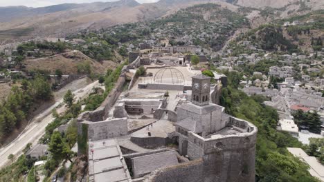 Aerial-view-of-tourists-visiting-Gjirokaster-Fortification-on-hilltop,-scenic-Clock-tower,-Albania