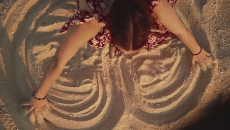 Overhead-close-up-shot-of-a-Caucasian-female-sitting-on-a-beach-drawing-a-large-heart-in-the-sand-using-her-hands