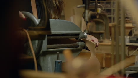 Young-female-shoemaker-cutting-shoe-leather-on-old-fashioned-workshop-equipment-close-up-slow-motion