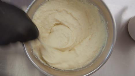 Top-down-establishing-shot-of-a-gloved-person's-hand-stirring-flour-dough-in-a-bowl
