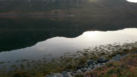Ein-Langsamer-Schwenk-über-Stilles-Wasser-In-Einem-Seeloch-In-Schottland,-Während-Die-Sonne-Hinter-Bergen-Untergeht