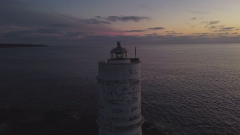 Majestic-aerial-of-Lighthouse-with-faded-paint-and-solar-panels,-shining-light
