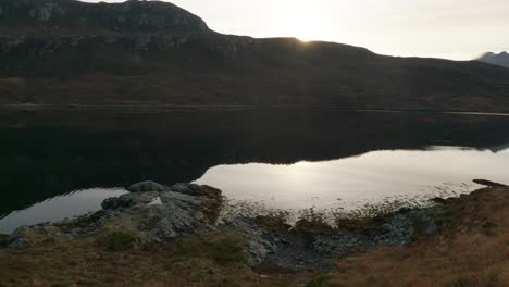 Eine-Langsame-Schwenkneigungsaufnahme-Von-Stillem-Wasser-In-Einem-Seeloch-In-Schottland,-Während-Die-Sonne-Hinter-Bergen-Untergeht