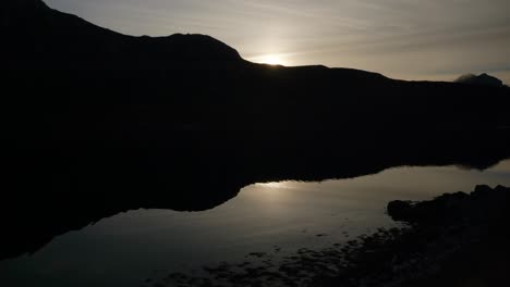 The-shadow-of-a-mountain-is-perfectly-reflected-in-the-water-of-a-Scottish-sea-loch-at-sunset-as-ripples-gently-move-across-the-water's-surface