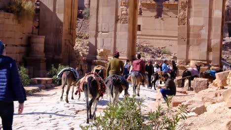 Arabian-people-riding-donkeys-over-stone-cobbled-path-through-Petra-in-Jordan,-Middle-East,-with-tourist-exploring-the-ancient-city
