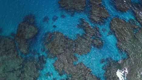 A-drone-captures-a-shot-of-a-blue-lagoon,-showcasing-the-crystal-clear-waters-that-you-can-see-the-rocks-and-the-bottom-of-the-sea,-offering-a-glimpse-of-the-natural-beauty-of-the-underwater-world