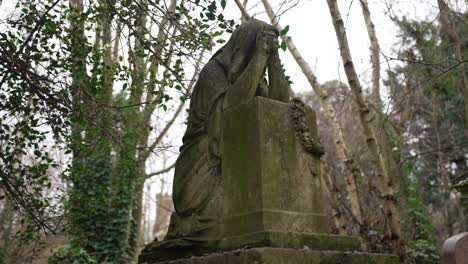 Betende-Statue-Auf-Einem-Bemoosten-Grabstein-Auf-Einem-Waldfriedhof-An-Einem-Bewölkten-Tag