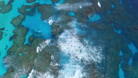 A-drone-captures-the-beauty-of-a-blue-lagoon-reef-with-crashing-waves-during-the-day,-showcasing-the-vibrant-colors-and-dynamic-movement-of-the-water