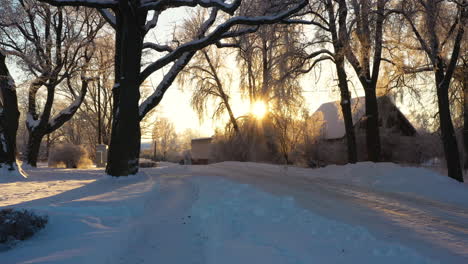 Scenic-snowy-farmhouse-driveway-with-glowing-sunset-shining-between-tree-branches-in-winter