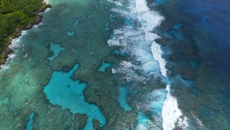 The-drone's-camera-pans-over-the-blue-lagoon,-capturing-the-stunning-transparency-of-the-water,-allowing-a-view-of-the-seabed-and-the-rocks-beneath,-while-the-waves-crash-on-the-reef