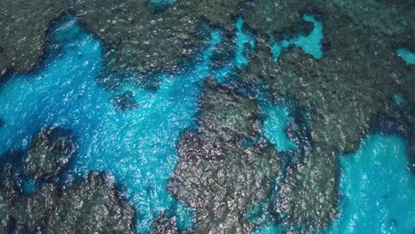 A-drone-captures-an-aerial-shot-of-a-blue-lagoon,-showcasing-the-crystal-clear-waters-that-reveal-the-stunning-underwater-landscape-of-rocks-and-marine-life-below